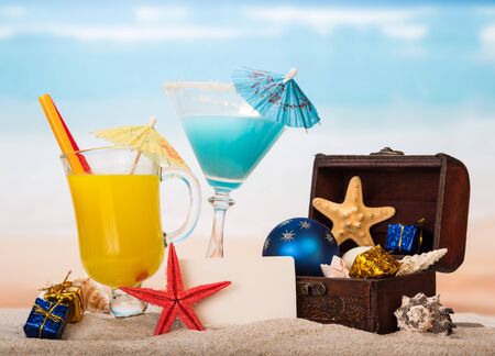 Blank card, cocktail, juice, starfish and treasure chest with presents in the sand against the sea.の写真素材