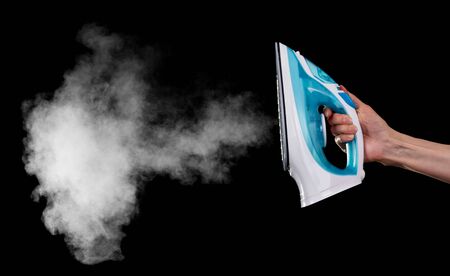 Steam iron in a female hand isolated on a black background.の写真素材