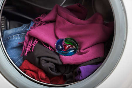 Drum of a washing machine close-up with dark laundry and a capsule of concentrated gel for washing