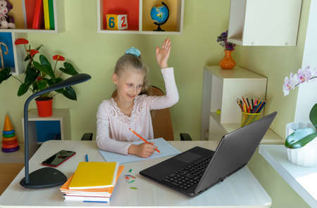 Distance learning concept. Girl communicates via laptop with her teacher while sitting at homeの写真素材