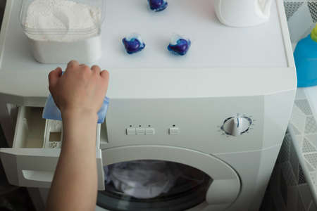 Bathroom. A woman's hand pours washing powder into the compartment of the machineの写真素材
