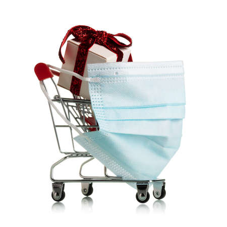 Personal protection mask on a wheelbarrow for shopping in a supermarket with bright new year gifts isolated on white backgroundの写真素材