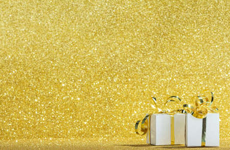 White gift boxes with ribbon on sparkling gold background with glitterの写真素材