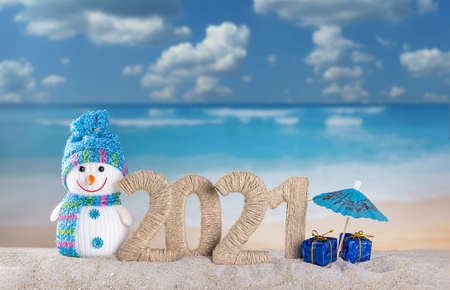 Merry Christmas and Happy New Year. Snowman and the inscription 2021 in the sand on the beachの写真素材