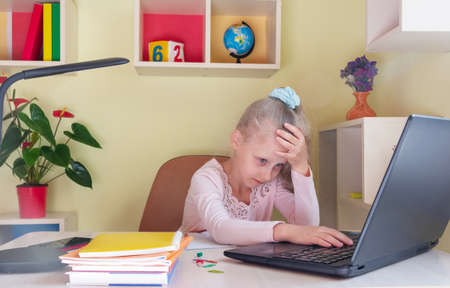 Sad schoolgirl is studying remotely on a laptop. Difficulties in perceiving information in remote learningの写真素材