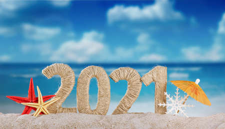 Concept of celebrating the new year in hot countries. The inscription 2021 in the sand and a snowflake under the snow on a bright day on the beachの写真素材