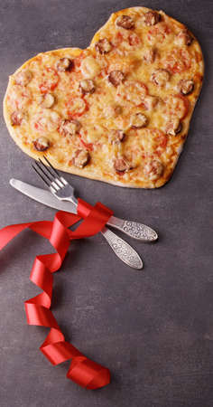 Valentine's day romantic dinner. Pepperoni pizza, cutlery and bright scarlet ribbon on dark tableの写真素材