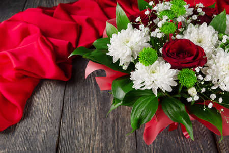 Bouquet of scarlet roses and chrysanthemums on a wooden background and fabricの写真素材