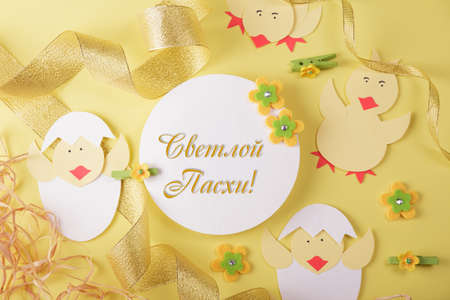 Inscription of light Easter in Russian. Easter card with chickens and golden ribbon on yellow backgroundの写真素材