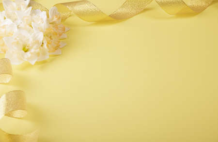 Fresh light daffodils and gold ribbon on a yellow background. Place for inscriptionの写真素材