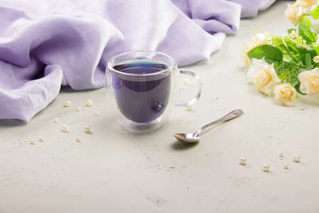 Healthy blue tea in a transparent cup and napkin on a light background with flowersの写真素材