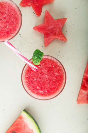 Juicy delicious watermelon smoothie in a glass decorated with mint and pieces of watermelon on a light backgroundの写真素材