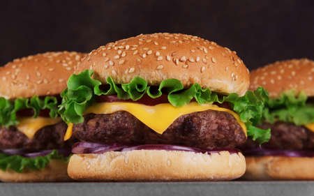 Three juicy tasty burgers close-up with salad and meat on a dark background