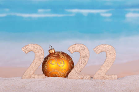 New Year concept. Lettering 2022 with bright christmas ball on the beach by the seaの写真素材