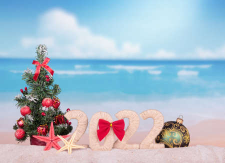 Christmas concept. New year 2022 sign with a Christmas tree and a large ball on a beach backgroundの写真素材