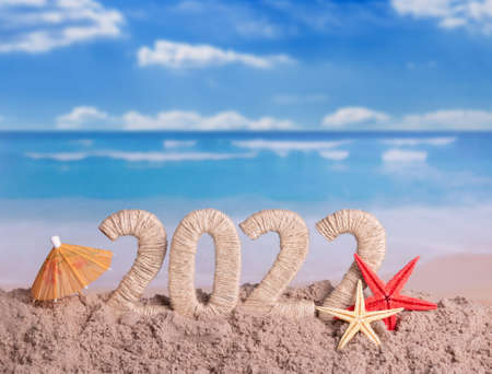 New year on the beach. The inscription 2022 in the sand, starfish and an umbrella on the background of the seaの写真素材