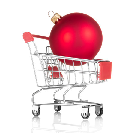 Concept of New Year's bustle and shopping. Christmas red ball in shopping cart isolated on white backgroundの写真素材