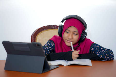 A young female muslim teenager using a tablet for studying online, isolated on white backgroundの写真素材