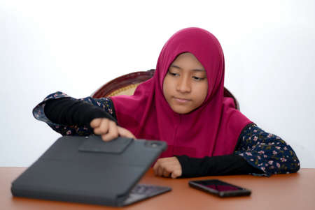 A young female muslim teenager using a tablet for studying online, isolated on white backgroundの写真素材