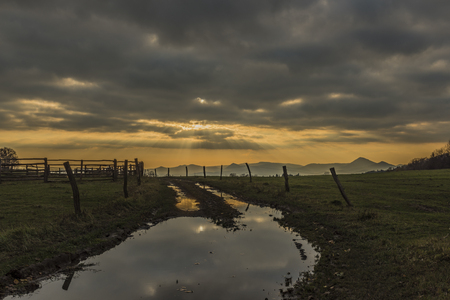 Path and fence near pasture land in Ceske Stredohori mountains with sunsetの写真素材