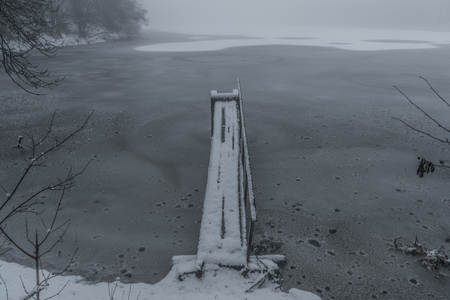 Frosty pond with mist and snow in dark white winter day near spa town Kynzvartの写真素材