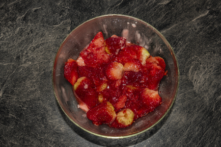 Making of young strawberries with sugar on black table in white tile kitchenの写真素材