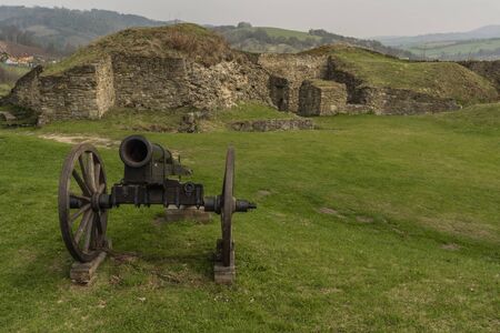 Cannon on green grass with stone wall in Brumov castle in spring cloudy day