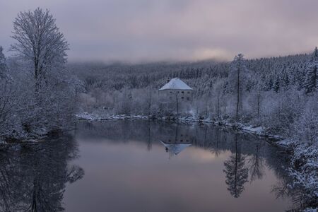 Blue cloudy snowy morning with fog and church in Loucovice village in south Bohemiaの写真素材