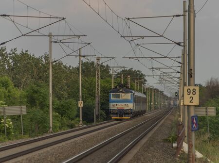 Electric blue engine and coaches on fast railway in south of Moravia in summer sunset evening
