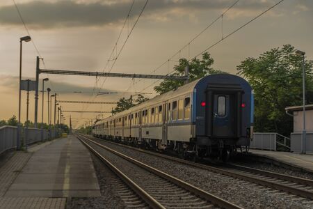Electric blue engine and coaches on fast railway in south of Moravia in summer sunset eveningの写真素材