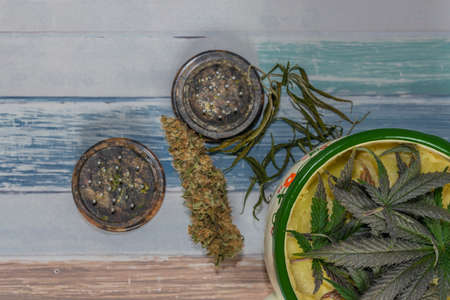 Metal color jug with marijuana yellow butter on wooden table with dry material and grinder