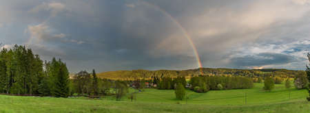 Rainbow over Bernov village in sunset evening with green fresh meadowsの写真素材