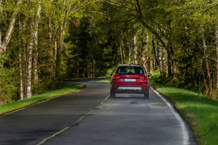 Red fast car in spring sunrise forest on wet black road after morning rainの写真素材