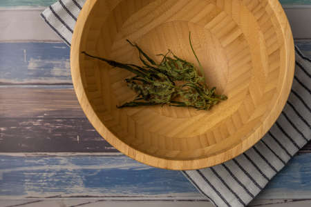 Wooden bowl with white striped dish towel and marijuana dry flower on color wooden table