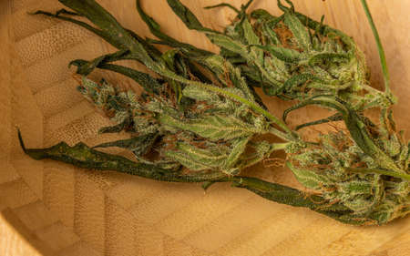 Wooden bowl with white striped dish towel and marijuana dry flower on dark wooden tableの写真素材