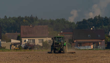 Green tractor with plow on brown field in autumn sunny color morningの写真素材