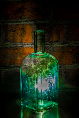Very old liquer glass green bottle with red brick and black backgroundの写真素材