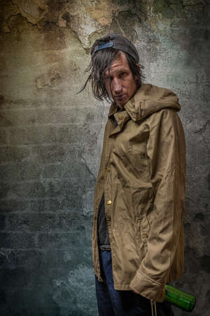 Junkie man with cap green anorak and blue sweatpants near stone old wallの写真素材