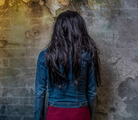 Black long hair woman in violet dress and jeans jacket near old stone dark wallの写真素材