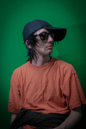 Man with black hair sitting near dark green wall