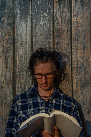 Black hair man sitting near old wooden wall with book in sunset hot evening