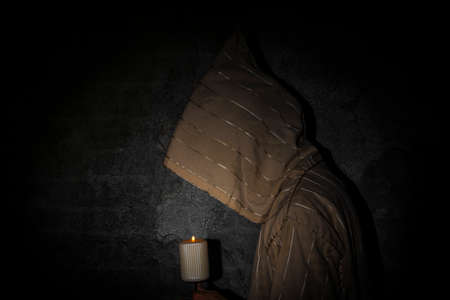 Tall man with long priest dress with stone old wall with candle