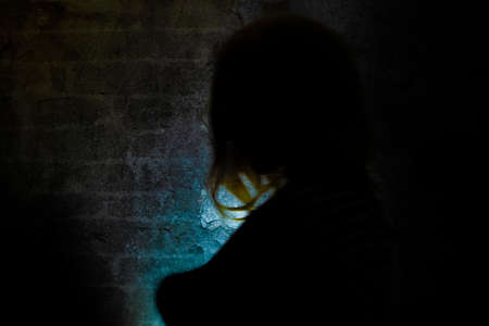 SIlhouette of blond hair woman near old stone dark wall