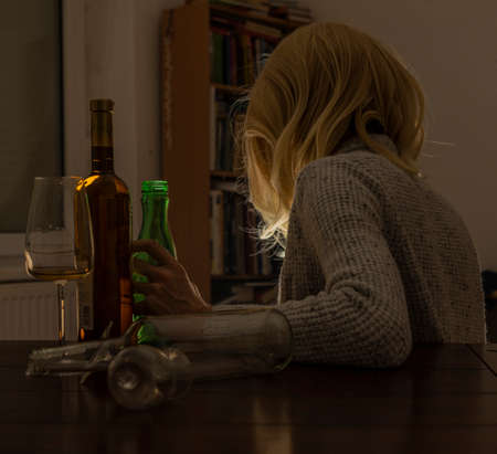 Blond hair woman with bottles of alcohol in dark interiorの写真素材