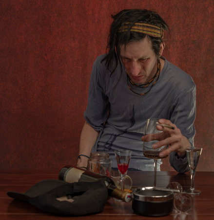 Dirty black hair man with alcohol glassess and bottles and dark red background