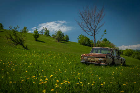 Very old broken car on spring color meadow near Banska Stiavnica town in sunny dayの写真素材