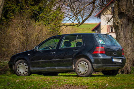 Black old dirty scratched car on morning meadow in fresh spring