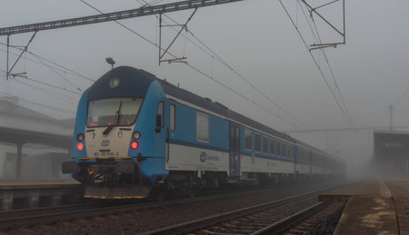 Commuter blue electric train in Kolin station in mist autumn cold morning