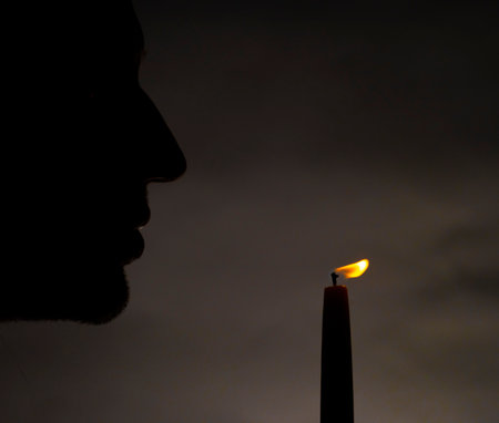 Silhouette of male with light of thin candle with dark background