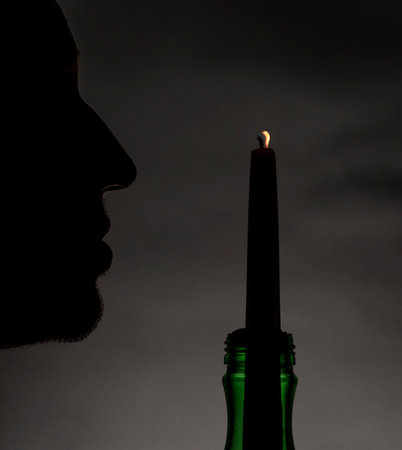 Silhouette of male with light of thin candle with dark backgroundの写真素材